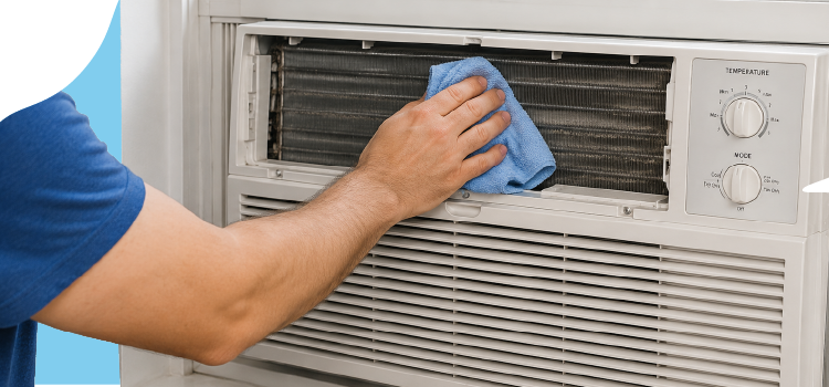 A person cleaning the metal coils of an indoor window air conditioning unit with a blue cloth. A-person-cleaning-the-metal-coils-of-an-indoor-window-air-conditioning-unit-with-a-blue-cloth